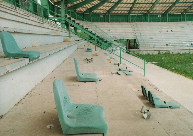 Ein Stadion mit wenigen Sitzplätzen, grasigem Boden und sichtbaren Stufen zum Hochsteigen.
