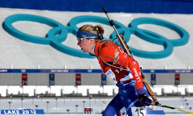 Lindsey Vonn in rot-blauem Skioutfit fährt eine schneebedeckte Piste hinunter und hält Ski-Stöcke in den Händen, mit Brettern mit Text und Zahlen im Hintergrund und einer gestalteten Wand.