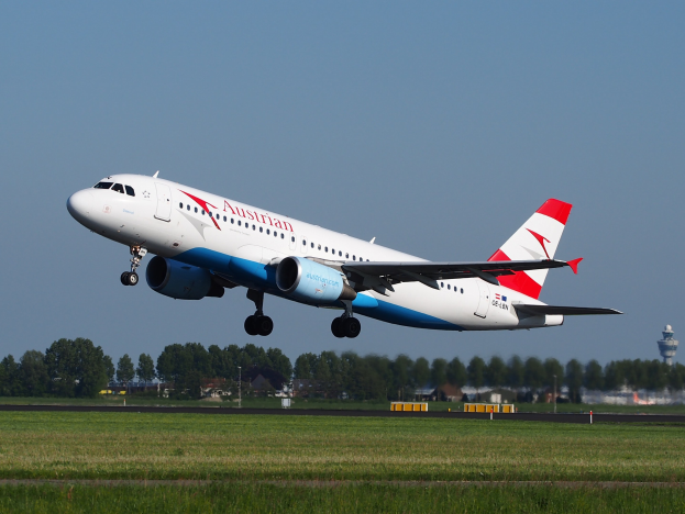 Airbus A320-200 der Austrian Airlines startet vom Frankfurter Airport mit grünem Gras darunter, Bäumen und Gebäuden im Hintergrund und einer Kontrollturm auf der rechten Seite.