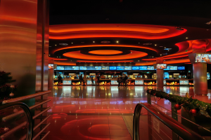 Ein Casino-Innenraum mit einem Weihnachtsbaum in der Mitte, gefliestem Boden, Geländern auf beiden Seiten, dekorierten Säulen, Deckenbeleuchtung und einer festlichen Menge im Hintergrund.