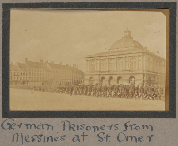 Gruppe deutscher Kriegsgefangener aus Messines vor einem Gebäude mit einem klaren blauen Himmel im Hintergrund, mit Text am unteren Bildrand.