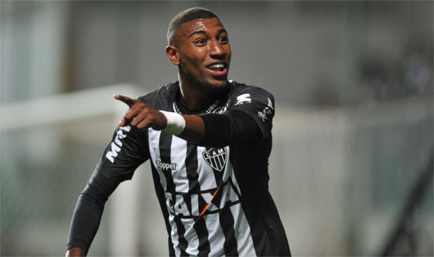 Ein Fußballer in einem schwarz-weißen gestreiften Trikot lächelt beim Feiern eines Tores, mit einem unscharfen Hintergrund.