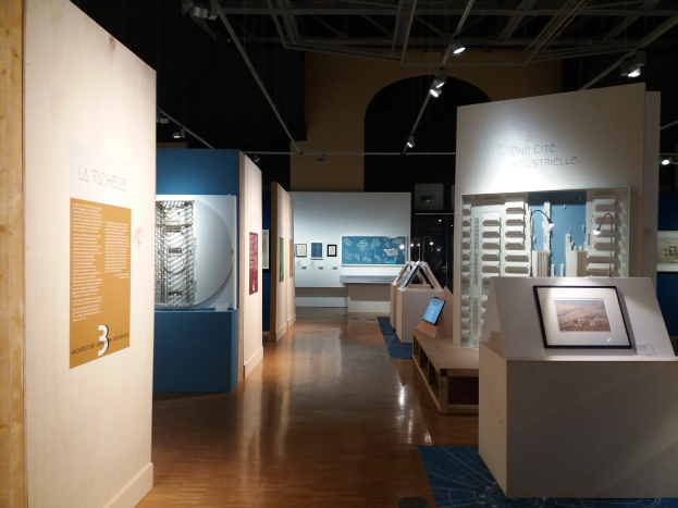 Ein Raum im Museum of Modern Art voller verschiedener Kunstwerke, darunter gerahmte Fotos auf Tischen, Texttafeln an den Wänden, Deckenleuchten und ein Teppichboden.