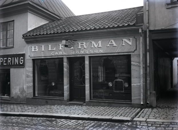 Ein Schwarz-Weiß-Foto eines Gebäudes mit einer "Bilferman"-Aufschrift, Fenstern, einer Tür und Schildern mit Text, mit einer Straße unten.