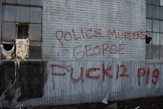 Graffiti auf einer Gebäudewand mit der Aufschrift "Polizei Mord George Fuck 12 P19" und Fenstern und verstreuten Gegenständen davor.