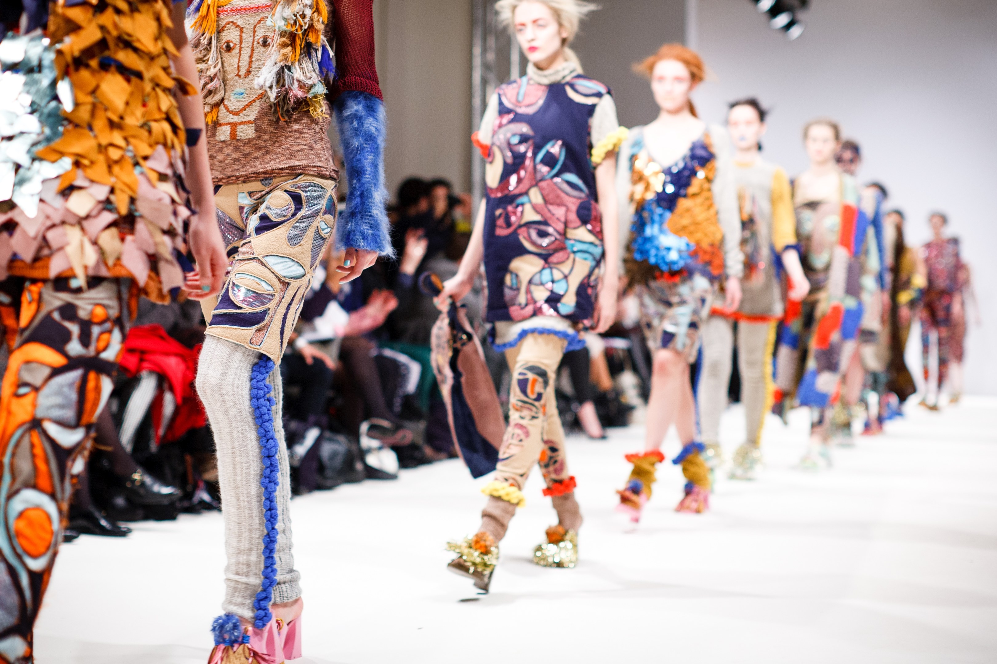 Eine Gruppe Von Frauen, Die Auf Einem Laufsteg In London Fashion Week Gehen, Mit Sitzenden Zuschauern Und Heller Beleuchtung Im Hintergrund, Erzeugt Eine Leichte Unschärfe, Träumerische Wirkung.