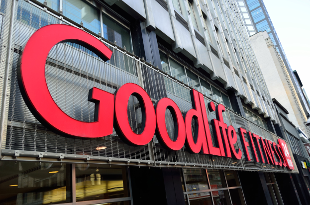 Ein Goodlife Fitness Studio in New York City mit Glaswänden und einem Namen auf dem Gebäude, flankiert von anderen Gebäuden und einem sichtbaren Himmel im Hintergrund.