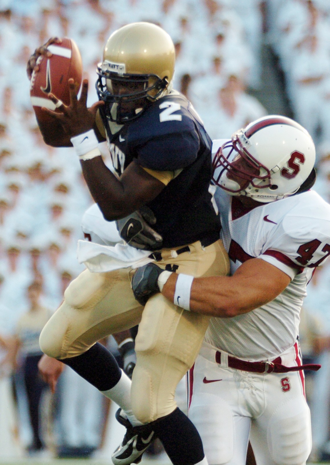 Zwei Fußballspieler in Sportkleidung und Helmen, einer fängt einen Ball in der Luft, während er von einem anderen getackelt wird, mit einem unscharfen Hintergrund.
