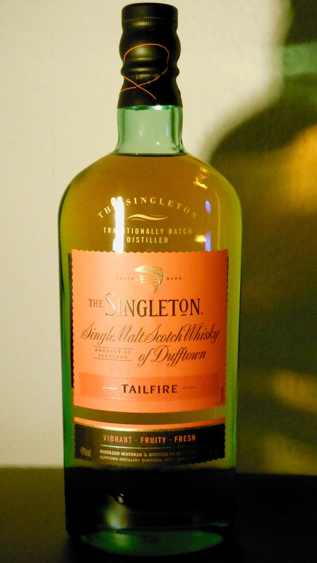 Eine tiefe bernsteinfarbene Flasche Singleton of Dufftown Tailfire Single Malt Scotch Whisky mit einer schwarzen Etikett, auf der in fetter Schrift der Name des Whiskys und ein Wappen mit einem Löwen und einem Schloss abgebildet sind.