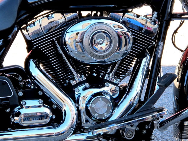 Eine Sammlung von Motorradteilen, darunter ein Motor, ein K├╝hler, ein Auspuffrohr, Zahnr├Ąder, St├Ąbe, Muttern und Dr├Ąhte.