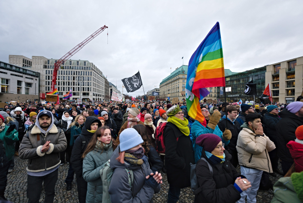 Eine große Gruppe von Menschen mit LGBTQ+-Rechten-Schildern und -Fahnen vor einem Gebäude mit einem Kran im Hintergrund.