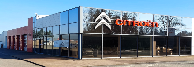 Ein Citroën-Autohaus mit Glaswänden und -türen, einer Straße davor und einem klaren blauen Himmel im Hintergrund.