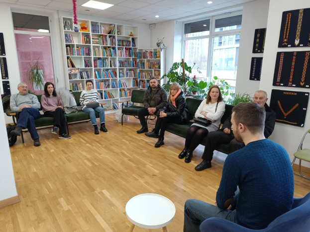Eine Gruppe von Menschen sitzt um einen Tisch in einem Raum mit Bücherregalen, Pflanzen und Deckenleuchten und ist in ein Gespräch vertieft während eines Workshops über die Zukunft von Gesundheit und Wohlbefinden in Berlin, Deutschland.