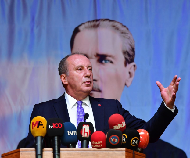 Ein Mann im Anzug und Krawatte steht hinter einem Pult mit Mikrofonen und spricht hinter einem Bildschirm, wahrscheinlich zu der Ankündigung des Rücktritts von türkischen Präsident Recep Tayyip Erdogan.