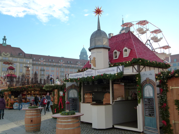 Ein geschäftiger Weihnachtsmarkt in Nürnberg, Deutschland, mit Menschen um geschmückte Stände, festlicher Beleuchtung, einem Riesenrad, Gebäuden mit Fenstern und einem bewölkten Himmel.