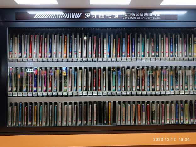 Eine gut beleuchtete Bibliothek mit hohen Bücherregalen voller Bücher, ein Textbrett und ein Wasserzeichen unten, das an eine Selbstbedienungsbibliothek in Stadtblöcken erinnert.