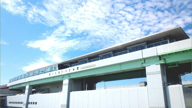 Ein Monorail-Zug fährt über eine von Säulen und Geländern getragene Brücke, mit Gebäuden und einem bewölkten Himmel im Hintergrund.