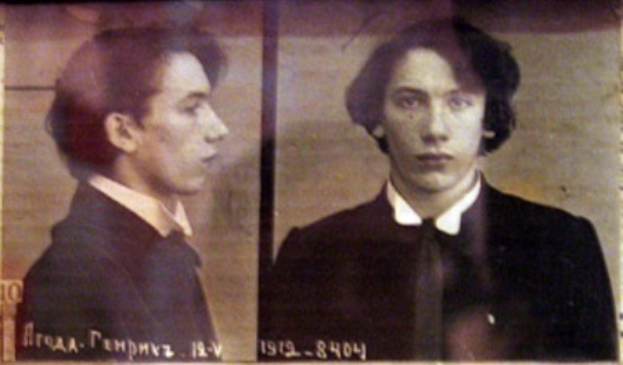 Ein Fahndungsfoto eines Mannes in einem schwarzen Anzug, weißem Hemd und schwarzer Krawatte mit ernstem Gesichtsausdruck, verschränkten Händen und zurückgekämmtem Haar, begleitet von zwei zusätzlichen Fotos und fettgedrucktem Text über seine Verbrechen.