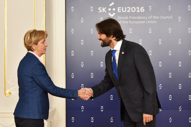Bundeskanzlerin Angela Merkel und Bundespräsident Joachim Gauck schütteln sich lachend vor einer Wand mit einem "EU-Gipfel"-Banner und einer Tür die Hände.