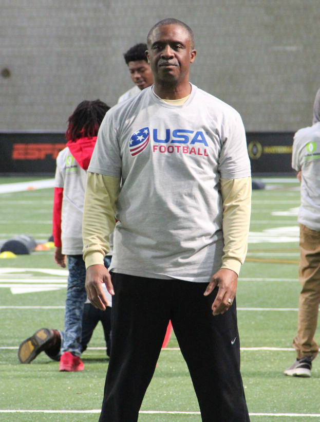 Ein Fussballspieler auf einem Feld mit einer Gruppe von Menschen und einer Wand im Hintergrund.