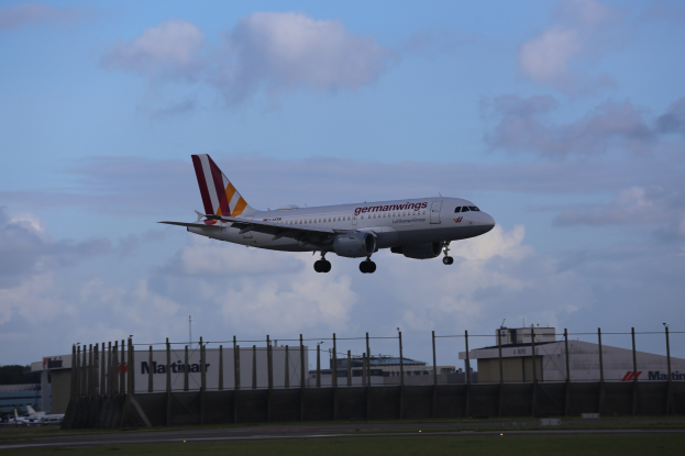 Germanwings Airbus A320-200 beim Start von Frankfurt Airport, mit Gras, einem Zaun, Gebäuden, Bäumen und einer bewölkten Himmel im Hintergrund.
