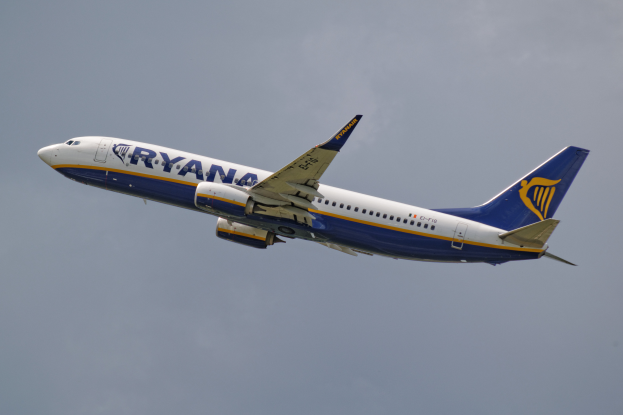 Ein Ryanair Boeing 737-800 Flugzeug mit weißer, blauer und gelber Lackierung im Flug gegen einen blauen Himmel, mit ausgebreiteten Flügeln.