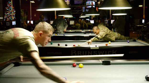Ein Raum mit Snookertischen, Spielern auf beiden Seiten, hängenden Lichtern, einem Weihnachtsbaum in einer Ecke und Bildschirmen mit Punkteständen.