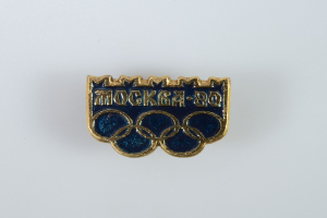 Ein blau-goldenes Abzeichen mit den Olympischen Ringen und einer Inschrift, die das 80-jährige Jubiläum der Olympischen Spiele in Moskau feiert, vor einem weißen Hintergrund.