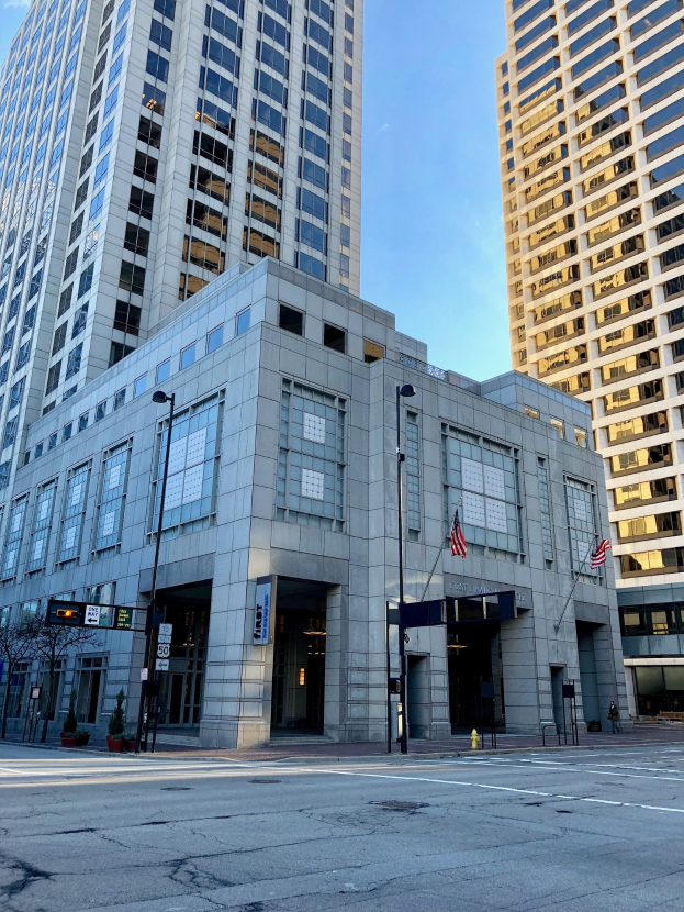 Großes Gebäude mit vielen Fenstern als Hauptquartier der Chicago Public Library identifiziert, das sich auf einer Stadtstraße befindet, umgeben von Straßeninfrastruktur und Bäumen unter einem bewölkten Himmel.