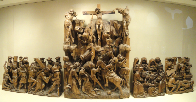 Eine Gruppe von Holzskulpturen, die in einem Museum ausgestellt ist und mit einer Wand im Hintergrund arrangiert ist.