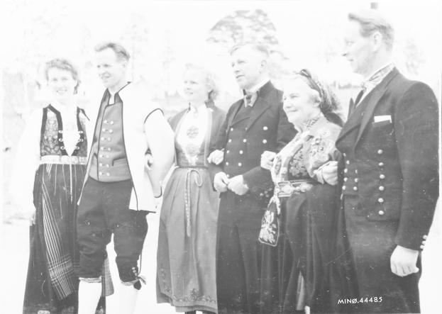 Eine Gruppe von Menschen aus den 1930er Jahren, die zusammenstehen, lächeln und von Bäumen umgeben sind, mit dem Text "Bayerische Familie in den 1930er Jahren" unten.