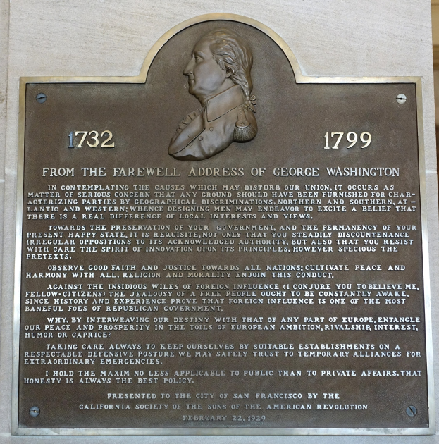Plaque an einer Gebäudeseite mit Text "Aus der Abschiedsrede von George Washington" und einer zentralen menschlichen Gesichtsplastik.