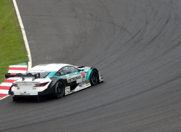 Ein Mercedes-AMG GT3 Rennauto auf einer Rennstrecke fahrend, mit Text auf dem Auto und Gras auf der linken Seite der Strecke.