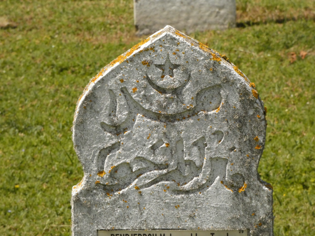 Grabstein mit arabischer Schrift in einem grünen Friedhof.