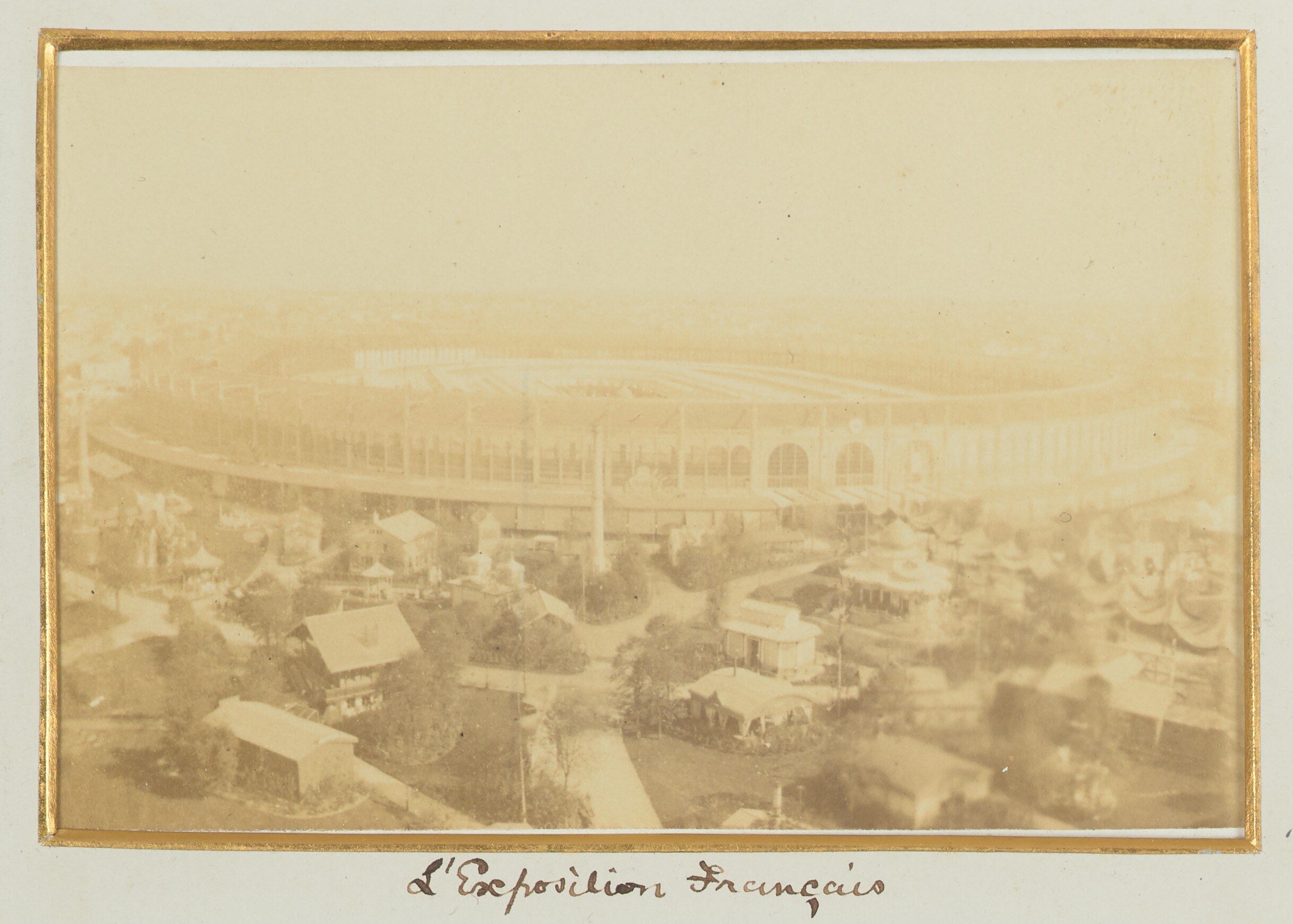 Altes Schwarz-Weiß-Foto eines Stadions inmitten einer Stadt, flankiert von Gebäuden, Bäumen und Strommasten, mit Text am unteren Rand.