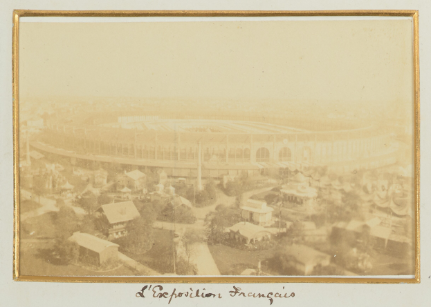 Altes Schwarz-Weiß-Foto eines Stadions inmitten einer Stadt, flankiert von Gebäuden, Bäumen und Strommasten, mit Text am unteren Rand.