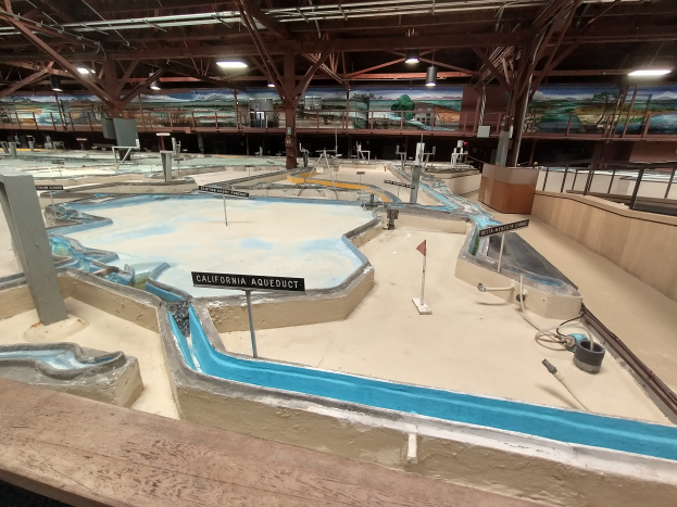Ein großer Indoor-Wasserpark mit zahlreichen Wasserbahnen, Pfählen, Texttafeln, Deckenleuchten und Wandgemälden, der wie ein Minigolfplatz gestaltet ist, um ein unterhaltsames und aufregendes Erlebnis zu bieten.