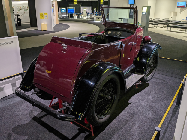 Alter roter Wagen in einem Museum mit umliegenden Ausstellungsstücken und Absperrungen.