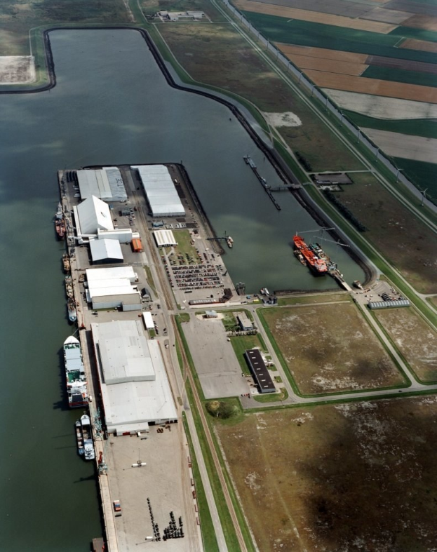 Luftaufnahme eines großen Gewässers mit einem Steg in der Mitte, umgeben von Gebäuden, Fahrzeugen, Straßen und Gras.