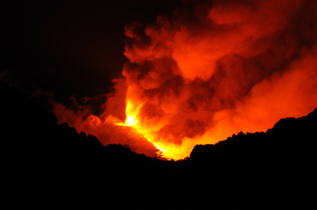 Ein Vulkan bricht nachts aus, mit leuchtend orangefarbenem und gelbem Lavafluss in den Ozean und Rauch, der in den dunklen Himmel aufsteigt.