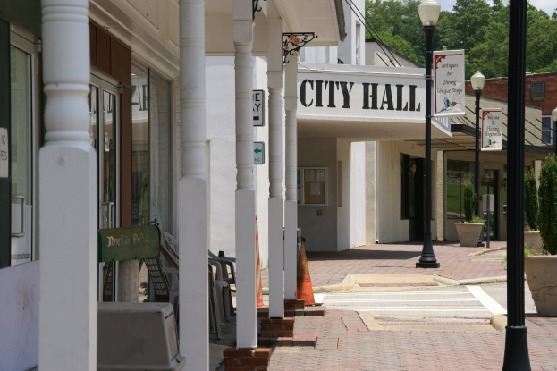 Stadtverwaltung mit Gebäuden, Straßenlaternen, Straßenschildern, Autos, Verkehrskegeln, Stühlen, Topfpflanzen, Bäumen und einem bewölkten Himmel im Hintergrund.