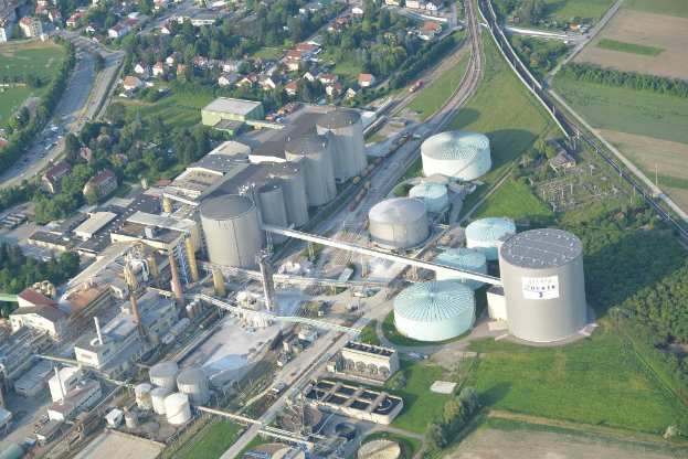 Luftaufnahme mit mehreren Gebäuden, Häusern, Bäumen und Fahrzeugen auf einer Straße umgeben von Gras.