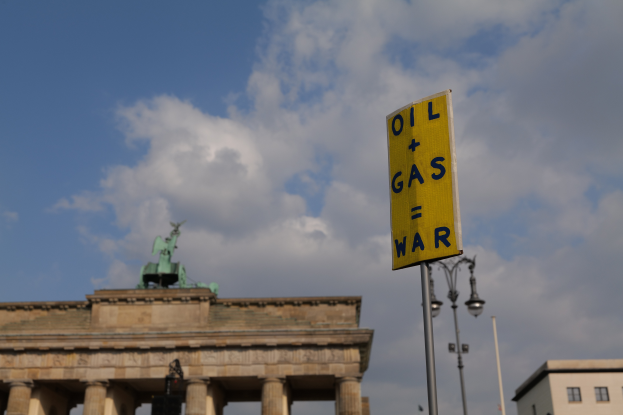 Das Brandenburgische Tor in Berlin, Deutschland, mit einem gelben Schild, das "Öl und Gas Krieg" liest, Gebäuden, Polen, Lichtern, einer Statue und einem bewölkten Himmel im Hintergrund.