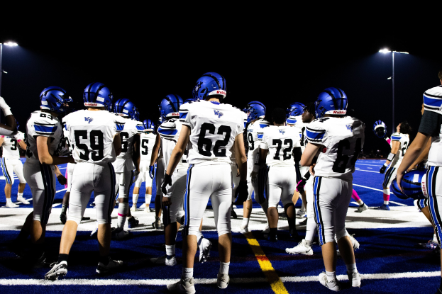Eine Gruppe von Fußballspielern in Helmen und Stollenschuhen steht auf einem Feld unter hellen Stadionlichtern und sieht bereit für ein Spiel aus.