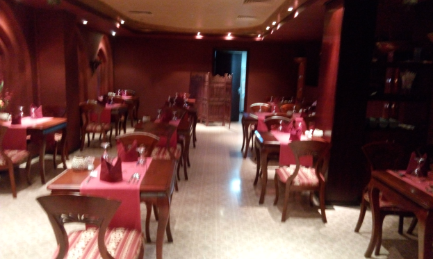 Ein Restaurant-Innenraum mit Tischen und Stühlen zum Essen, geschmückt mit Blumenvasen, Servietten und Besteck, mit Wänden, die mit Lichtern geschmückt sind.