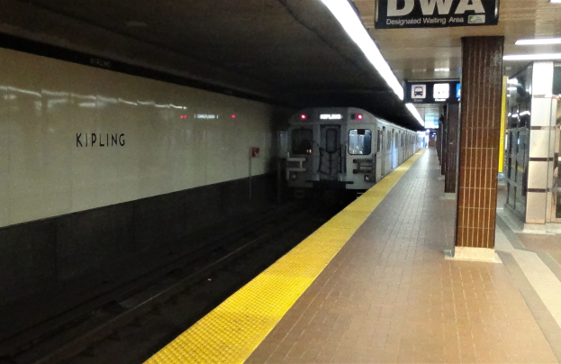 Eine U-Bahn fährt in einen Bahnhof ein, neben einem Bahnsteig mit einer Anzeigetafel darüber.