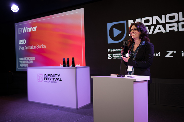 Eine Frau in einem schwarzen Kleid steht an einem Podium und hält eine Auszeichnung, mit einem Mikrofon und anderen Gegenständen auf dem Podium und einem Werbeplakat und einer Leuchte im Hintergrund bei den Monolux Awards 2020.