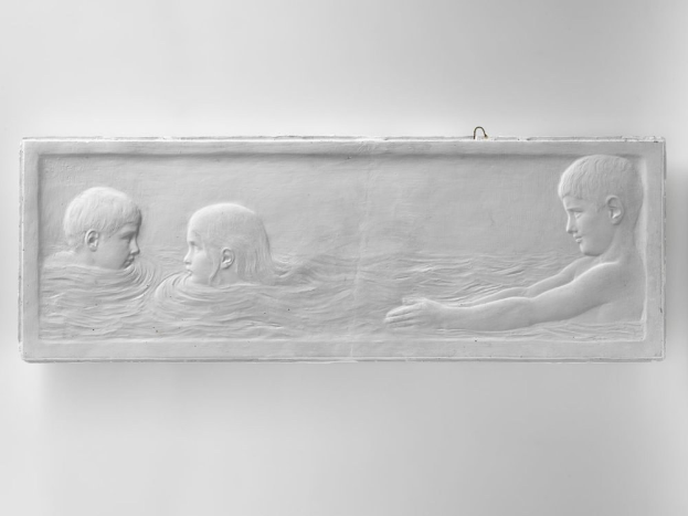 Drei Kinder schwimmen in einem Gewässer mit einer Wand im Hintergrund.