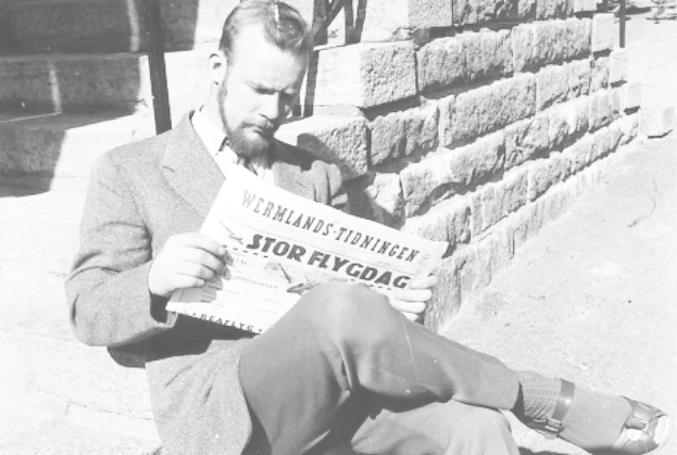 Ein Mann in einem Anzug sitzt auf den Stufen eines Gebäudes und liest eine Zeitung mit einem ernsten Gesichtsausdruck in einem Schwarz-Weiß-Foto.