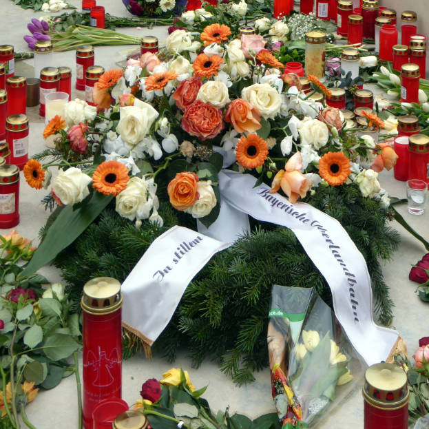 Mahnmal in Berlin mit Blumen und Kerzen vor einer Wand.